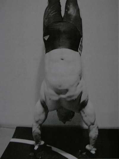 Brooks Kubik holding an extended handstand position while his upper-body muscles bulge.