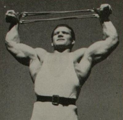 John Grimek extending a cable expander with arms overhead.