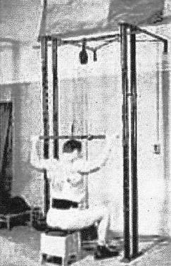 John Gremik doing lat pull-downs using a pulley wheel device attached to a chinning bar in a power rack.